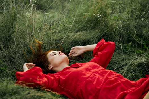 pretty woman in red dress lies on the grass in the field nature fresh air. High quality photo