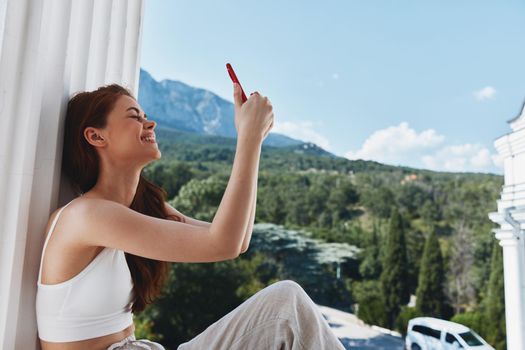 pretty woman sitting on the balcony with phone beautiful mountain view summer unaltered. High quality photo