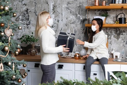 Beautiful mother and daughter in medical masks have fun at home near the Christmas tree in a interior. Family happiness, holiday, joy, vacation, games with a woman. New Year's preparations.