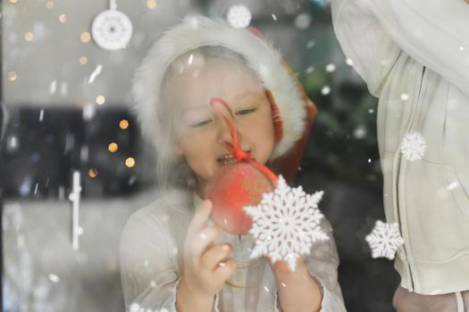 A girl wearing a santa claus hat looks at snowflakes on a window