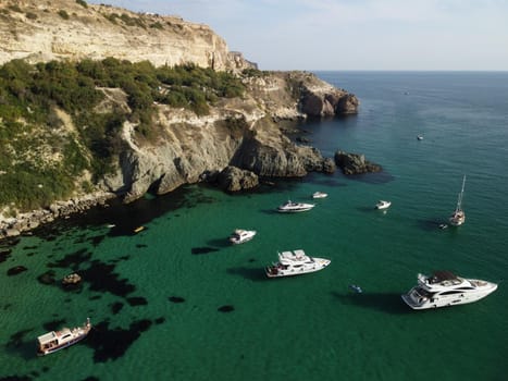 Sea landscape with rocky coastline on sunset time with cloudy sky. Yachts in the Sea on a background of rocky shores. The concept of perfect place for summer travel and rest.