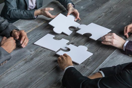 Hands of multi-ethnic team assembling jigsaw puzzle, multiracial group of black and white people joining pieces at desk, successful teamwork concept, help and support in business, close up view