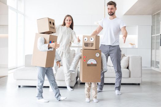 Happy family of parents and two children playing dancing like robots at home, children wearing handmade moving box costume of cardboard