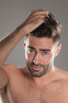 A portrait of a young handsome naked model man touching his hair