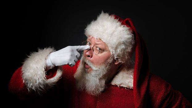 Funny Santa Claus wearing red costume adjusting glasses while standing over black background