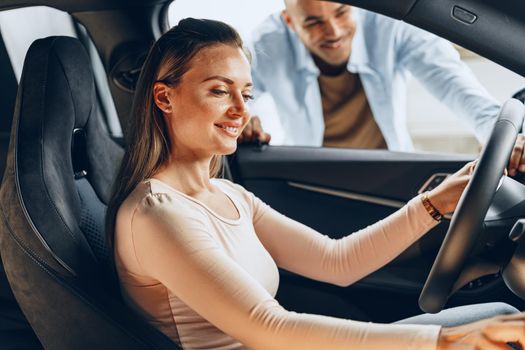 Joyful young couple looking around inside a new car they are going to buy in a car shop dealership