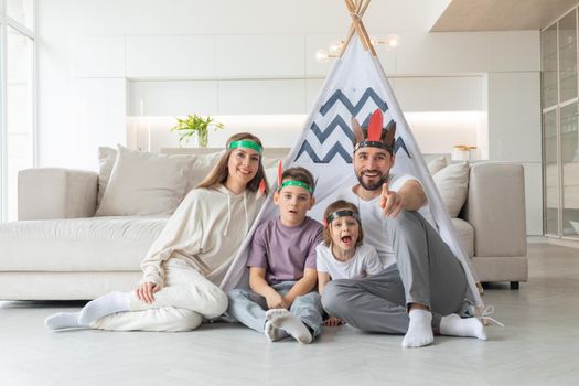 Happy young family having fun in living room at home. Mother, father, sister and brother playing together in wigwam