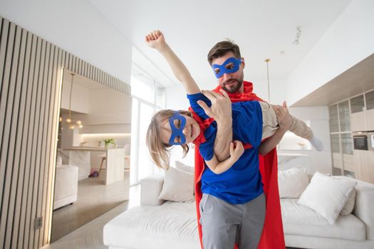 Father holding son flying in superhero costume at home