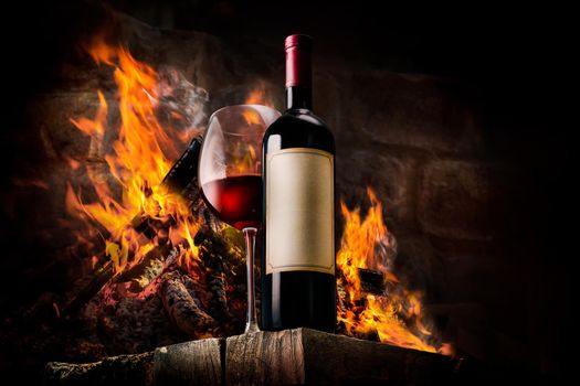 Glass and bottle of red wine on fire background
