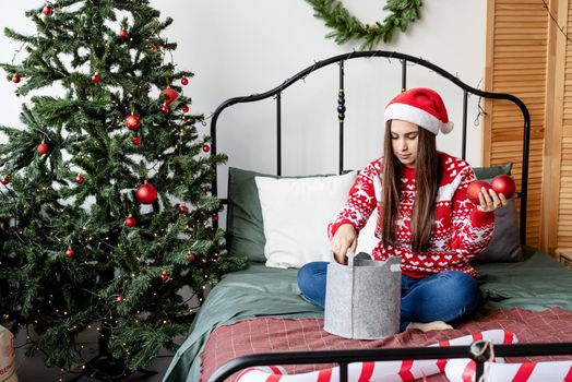 Merry Christmas and Happy New Year. Happy young woman in red sweater and santa hat sitting on the bed celebrating christmas