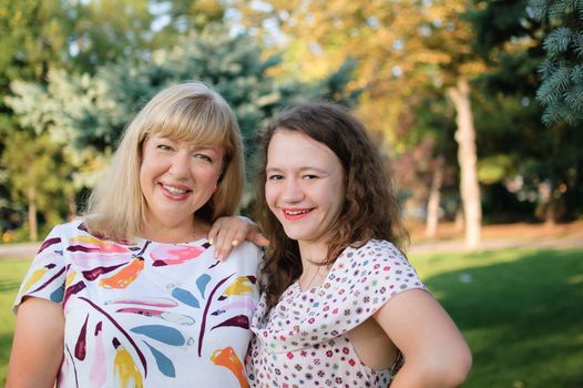 Female portrait of a beautiful plus size blond, blue-eyed mother and daughter in the park during summer. Family day, happy people concept.