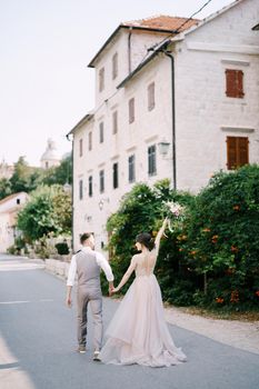Bride and groom walk down the street past the old building. Back view. High quality photo