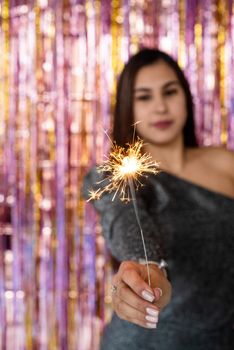 New Year party celebration. woman in glitter dress holding sparkler, close up hands, romantic look on purple and gold glitter background
