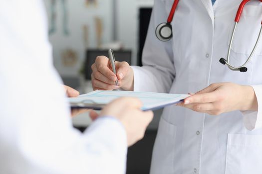 Close-up of doctor in medical gown put sign on clipboard with prescription paper. Qualified worker made prescription for patient. Medicine, clinic concept