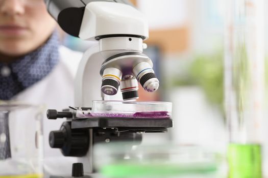 Close-up of woman scientist explore purple sample under microscope in laboratory. Smart chemist or biologist in office. Lab, science, investigation concept