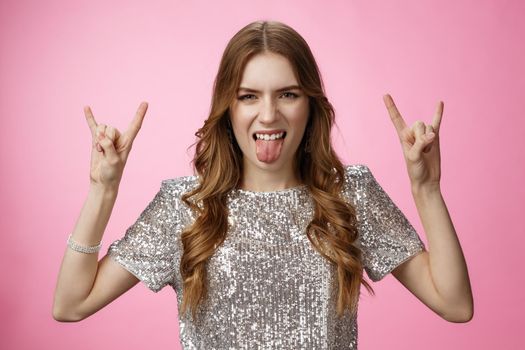 Close-up rebellious daring sassy attractive joyful cool woman having fun dancing enjoying party showing tongue making heavy metal rock-n-roll gesture relaxing listening awesome music, pink background.