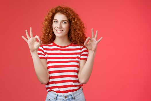 Fine relax everything perfect. Satisfied good-looking redhead cheerful sassy girlfriend curly haristyle show okay ok confirm gesture smiling approval agree good terms stand red background.