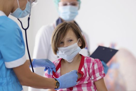 Portrait of girl being examined by pediatrician doctor with stethoscope tool. Calm little girl sit in office and get checkup. Medicine, appointment concept