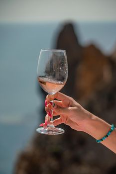 A female hand holds a glass of wine against the background of the sea and mountains