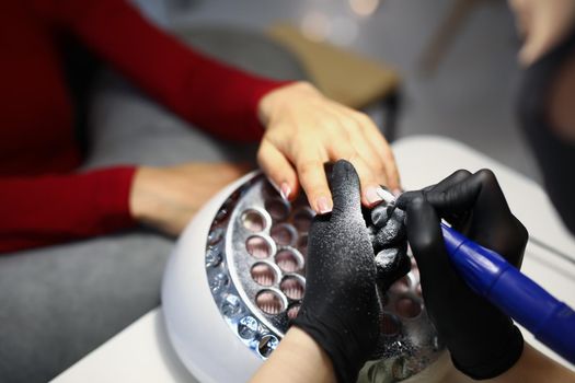 Close-up of nail master use special equipment for working with clients manicure. Professional beauty salon treatment for women. Self care, wellness concept