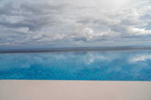 Infinity pool with sea and ocean views on the background of the sky with clouds. The clouds are reflected in the pool