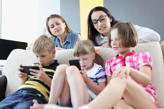 Portrait of kids play online games on mobile phones and mums control watching them. Addiction to smartphone from young age. Childhood, technology concept
