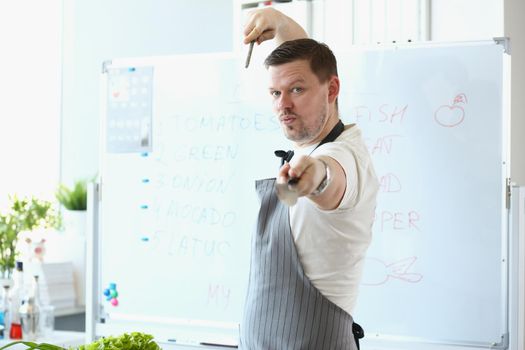 Portrait of attractive male chef standing in apron and pretend hes fighter with cooking knife. Blogger chef discover healthy eating habits. Food concept