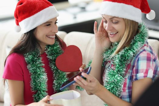 Portrait of woman got present smartphone from sister in heart shaped box. Happy woman shocked and cheerful at same time. New year, christmas, fun concept