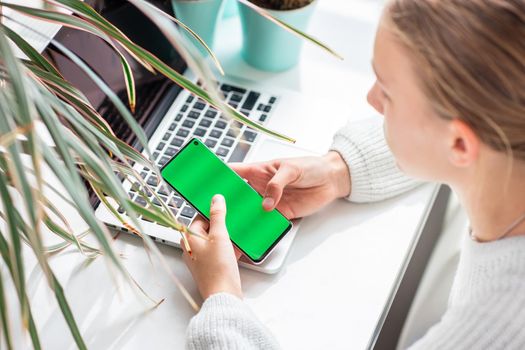 Beautiful teenage young school girl working at home checking her phone with chromakey, green screen in her room with a laptop studying in a virtual class. Distance education and learning concept during quarantine