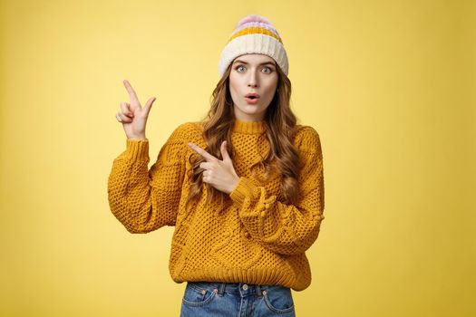 Amazed speechless stunned cute fashionable girl fold lips say wow widen eyes surprised impressed pointing upper left corner curious what promotion shows, look you questioned, yellow background.