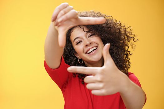 Portrait of optimistic happy and creative female student imaging her new apartment as extending hands and showing frames gesture smiling through it at camera amused and carefree over yellow wall.