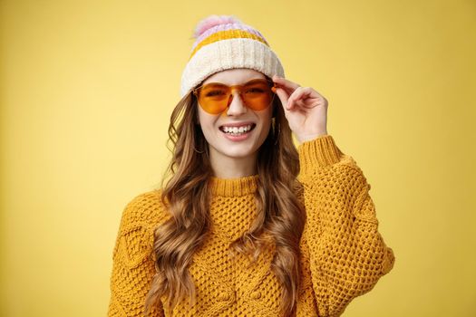 Friendly-looking happy outgoing attractive girl laughing joyfully having funny interesting conversation checking sunglasses relaxing ski resort having fun resting together friends, yellow background.