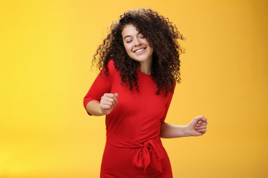 Carefree woman dancing on dance floor with close eyes and smile enjoying life feeling happy and joyful close eyes and making tender expression as moving to rhythm of music over yellow background. People, lifestyle and emotions concept