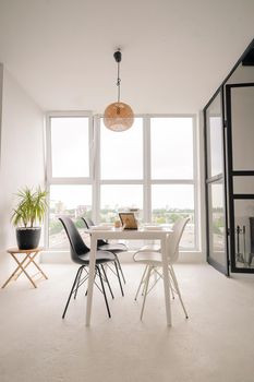 White Square Dinning Table Served for 4 Persons with Black and White Chairs in the Middle of the Bright Dinning Room. White Dinning Room with Light Walls and Floor, Big Window Frame, Elements of Decor. High quality photo