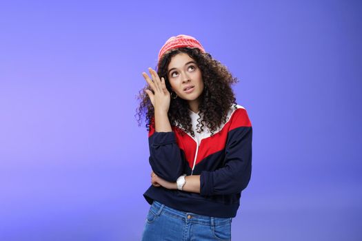 Waist-up shot of bored and annoyed assertive arrogant cool girl in streetstyle outfit rolling eyes up making facepalm and grimacing from irritation and disappointment, posing against blue background.