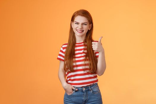 Cheerful friendly woman red natural hair clean skin, show thumb up, smiling approval, support perfect choice, like excellent performance, express positive opinion, acceptance, orange background.