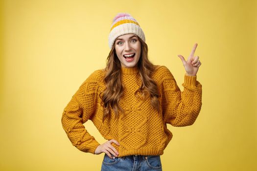 Amused friendly outgoing young girl having fun talking friends amused discussing cool promo pointing upper right corner smiling happily talking casually thrilled look camera, yellow background.