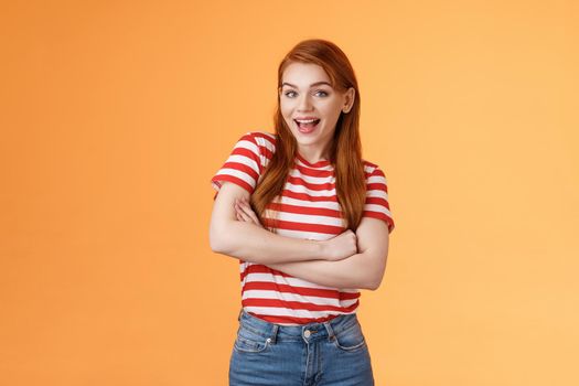 Excited cheerful ginger girl long natural red hair open mouth enthusiastic smile, cross arms chest, gladly react interesting awesome news, feel surprised pleased, stand orange background.