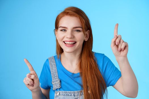 Close-up cheerful carefree redhead dancing girl pointing up, raising fingers, smiling amused, having fun, stand blue background entertained, enjoy music party, disco mood, carefree emotions concept.