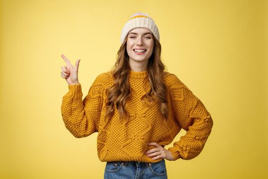 Confident fashionable 20s girl proudly smiling hold hand waist self-assured pointing upper left corner showing perfect copy space top advertisement, promoting product grinning delighted.