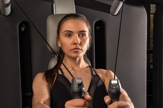 A woman engaged in fitness sits on the simulator, a young sports girl is engaged in sports