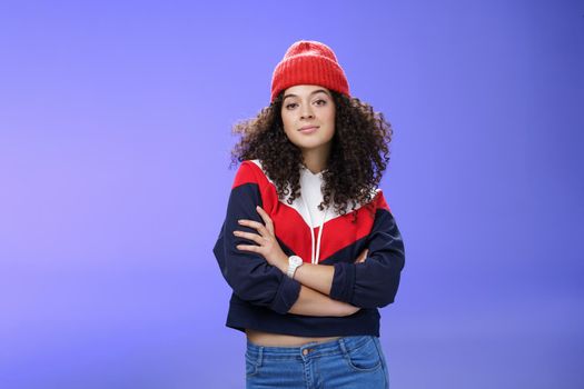 Girl will show winter who boss. Confident and stylish self-assured attractive woman with curly hair in cute red beanie and warm sweatshirt holding hands crossed over chest and looking daring at camera. Fashion, weather and people concept