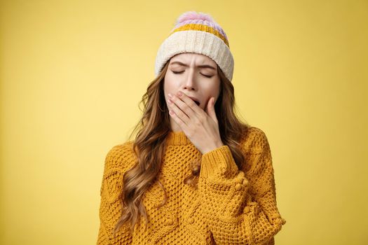 Close-up shot tired yawning cute exhausted european woman wearing hat sweater cover opened mouth feel sleepy drained wanna lay-down take nap, not morning person, yellow background.