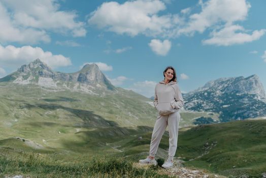 Hiker tourist girl standing on top of the mountain and enjoying valley view. Happy woman with her arms outstretched, freedom and happiness, achievement in mountains.