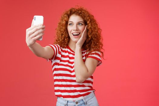 Fashionable cute redhead curly female summer t-shirt record video social media from luxury tropical resolt travel holidays abroad take selfie hold smartphone pose silly photograph red background.