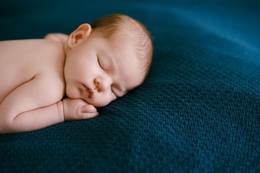 Naked baby sleeping on a blue blanket with his hand under his cheek. High quality photo