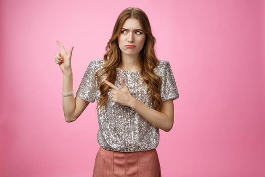 Displeased arrogant snobbish young rich glamour girl looking displeased cringe pointing left sideways, dislike place standing awkward insecure, expressing aversion reluctance, pink background.