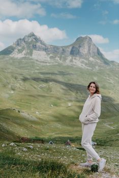 Hiker tourist girl standing on top of the mountain and enjoying valley view. Happy woman with her arms outstretched, freedom and happiness, achievement in mountains.