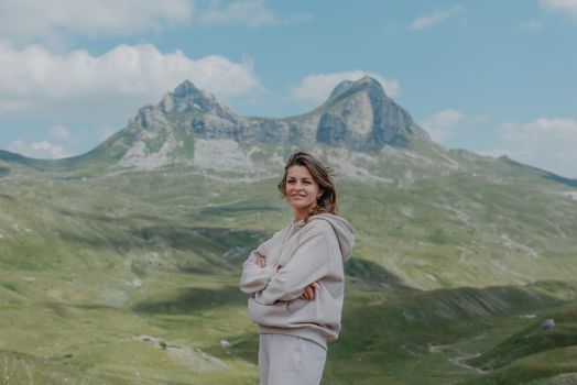 Hiker tourist girl standing on top of the mountain and enjoying valley view. Happy woman with her arms outstretched, freedom and happiness, achievement in mountains.