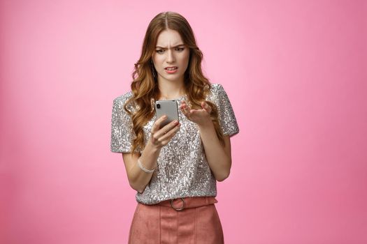 Frustrated pissed woman keep receiving strange messages cringing grimacing bothered look smartphone display gesturing irritated confused, cannot understand article, pink background. Copy space